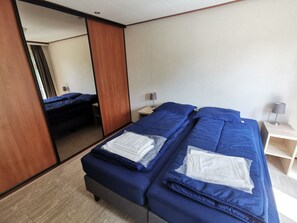A hotel room with two beds, a mirror, a bedside table with a lamp, and a wooden floor. - Comfort 3 Persons (Egmond aan den Hoef)