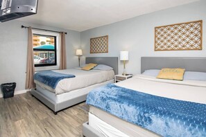 A hotel room with two beds, a window with a view of parked cars, a trash bin, and decorative wall panels. - 1915 Beach Club - Seaside Suite 8 (Daytona Beach)