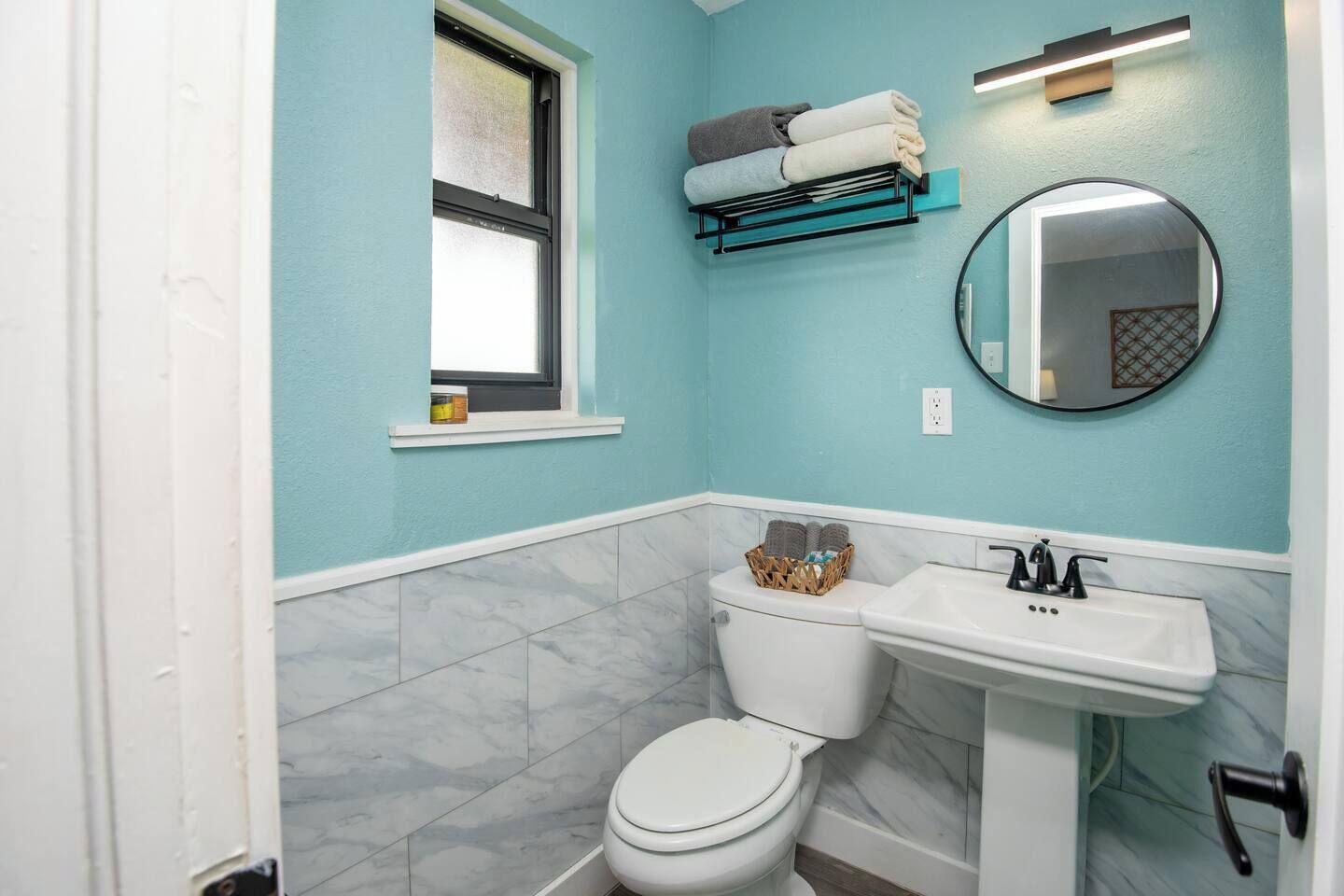 A bathroom with a toilet, sink, and a window.