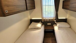 A compact room with two single beds, a window with curtains, and built-in wooden cabinets. - Holiday Home With 1 Bedroom (Berg en Terblijt)