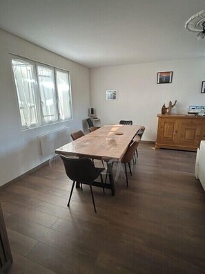 Ein geräumiger Raum mit großem Holzesstisch, Stühlen, einem Holzschrank und einem Fenster, das für natürliches Licht sorgt.