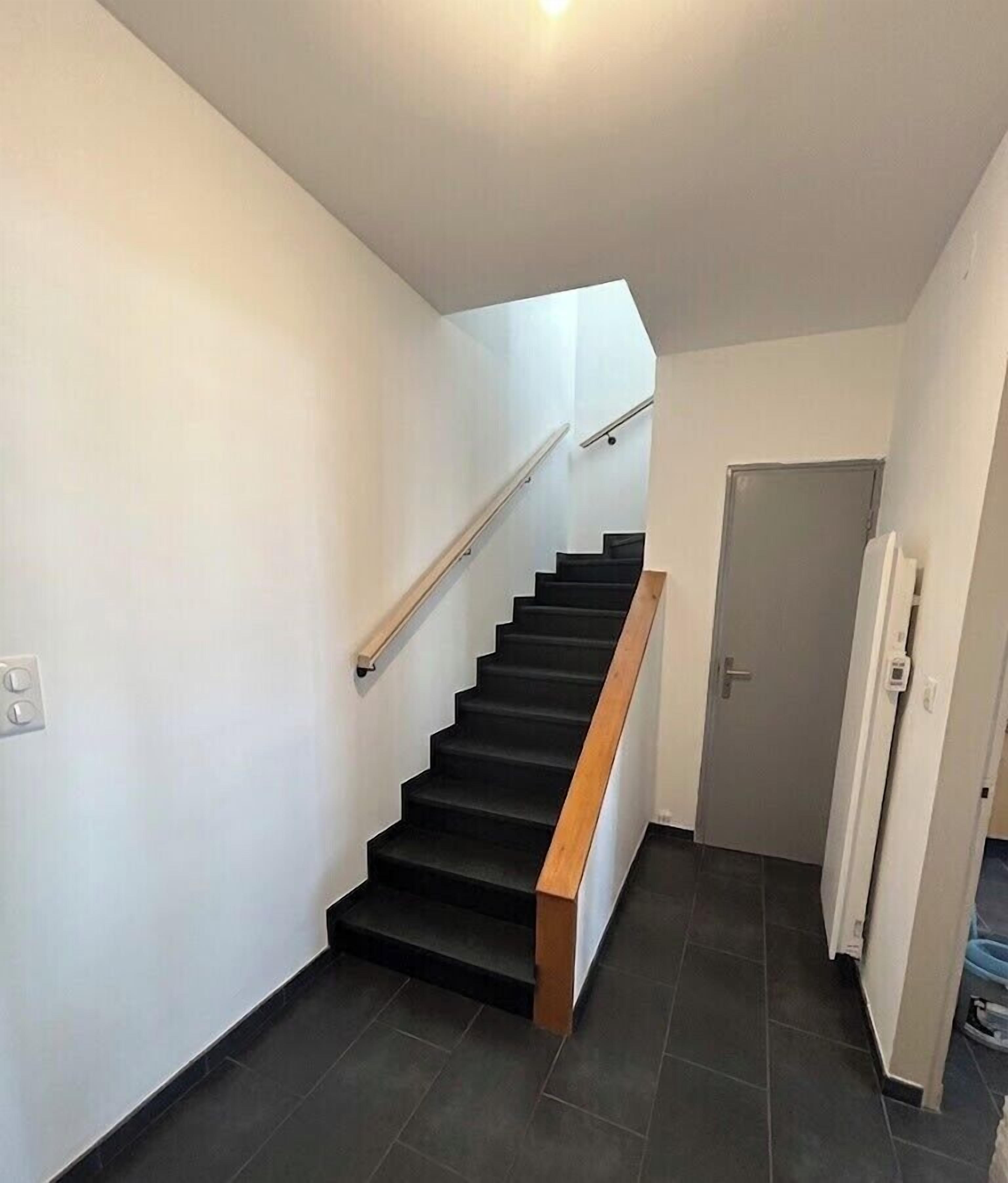 Una escalera con barandilla de madera, una puerta al final y una lámpara en el techo.