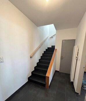 A staircase with a wooden handrail, a door at the bottom, and a light fixture on the ceiling. - "Les Chaumes" Country Cottage (Saint-Agnant)