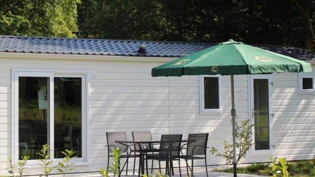 A white mobile home with a tiled roof, a sliding glass door, and a patio with a table and chairs. - Holiday Home in Susteren With Terrace (Susteren)