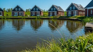 Una hilera de casas junto a una masa de agua tranquila, probablemente un canal, con un área verde al frente.
