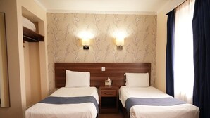 Ein Hotelzimmer mit zwei Betten, einem Nachttisch, einer Wandleuchte und einem Fenster mit Vorhängen.