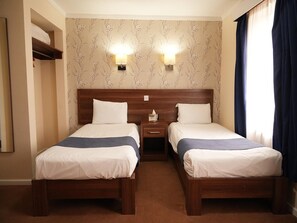 Ein Hotelzimmer mit zwei Betten, einem Nachttisch, einer Wandleuchte und einem Fenster mit Vorhängen.