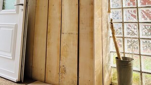 Een houten interieur met een bord waarop 'VENT OUEST RAFALF' staat, een deur en een raam met uitzicht.