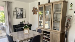A dining area with a wooden table, black chairs, a cabinet with glass doors, and a potted plant. - HOUSE IN THE MEYRAN NEIGHBORHOOD NEAR LA HUME (Gujan-Mestras)