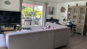 A living room with a sofa, television, and a sliding glass door leading to an outdoor area. - HOUSE IN THE MEYRAN NEIGHBORHOOD NEAR LA HUME (Gujan-Mestras)