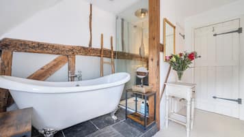 A bathroom with a freestanding bathtub, a wooden beam, a small table with a vase, and a door with a handle.