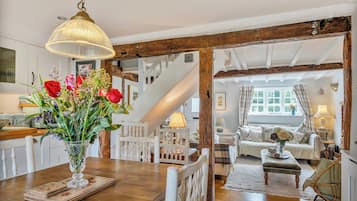 A rustic interior with a wooden staircase, a dining area with a vase of flowers, and a cozy living room with a sofa and lamp.