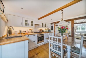 A kitchen with white cabinets, a wooden countertop, a dining table with chairs, and a hanging light fixture. - Windmill Cottage Sleeps 4 With Enclosed Garden (Henley-on-Thames)