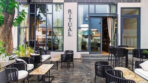 An outdoor seating area with tables and chairs, a tree, and a building with a sign that reads 'RITUAL.' - Solaris Luxury Residence | Osu • Pool • Gym (Accra)