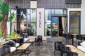 An outdoor seating area with tables and chairs, a tree, and a building with a sign that reads 'RITUAL.' - Solaris Luxury Residence | Osu • Pool • Gym (Accra)