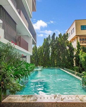 A swimming pool surrounded by lush greenery and modern buildings. - Solaris Luxury Residence | Osu • Pool • Gym (Accra)