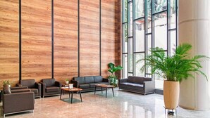A modern lobby with a wooden panel wall, leather sofas, a coffee table, and a large potted plant. - Solaris Luxury Residence | Osu • Pool • Gym (Accra)