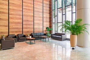 A modern lobby with a wooden panel wall, leather sofas, a coffee table, and a large potted plant. - Solaris Luxury Residence | Osu • Pool • Gym (Accra)