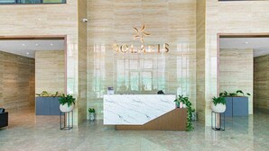 A reception desk with a marble top, a sign above it, and potted plants on either side. - Solaris Luxury Residence | Osu • Pool • Gym (Accra)