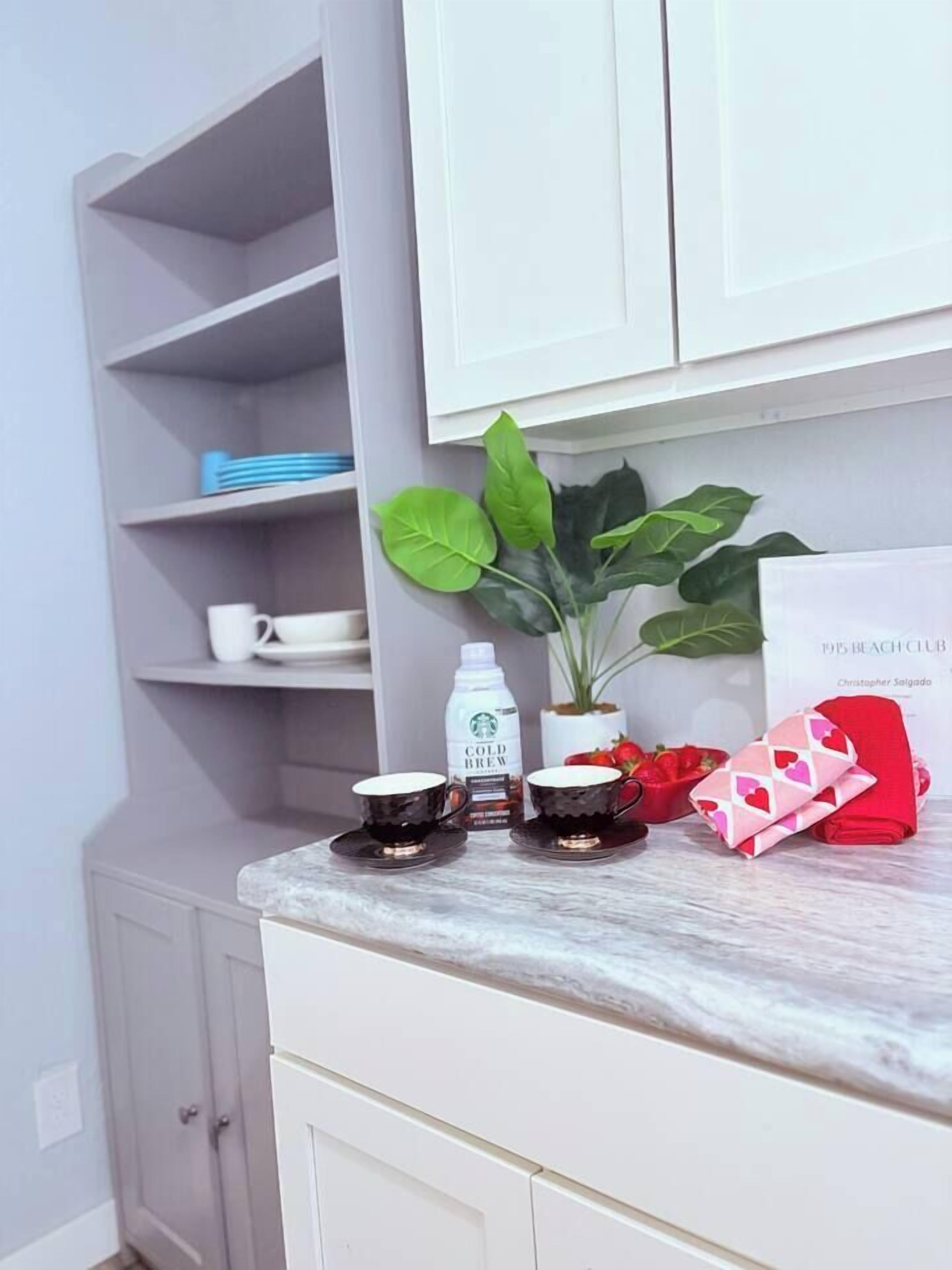 Una encimera de cocina con una cafetera, tazas, una planta y una caja de regalo roja.