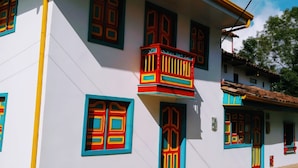 Um edifício com fachada branca, várias janelas com molduras coloridas e uma varanda com guarda-corpo vermelho.