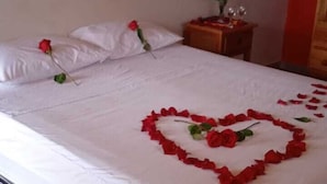 Cama com lençóis brancos e um arranjo de rosas em formato de coração sobre o edredom.