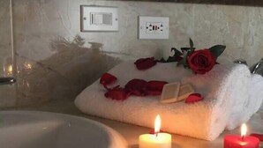 Um banheiro com uma banheira, uma toalha com pétalas de rosa e uma rosa, e três velas acesas.