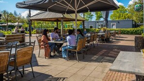 An outdoor patio with tables and chairs, a covered seating area, and a building in the background. - Holiday Home in Velsen-zuid With Terrace (Velsen-Zuid)