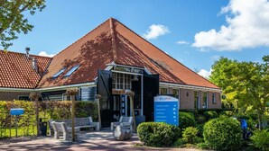 A building with a red-tiled roof, a signboard with directions, and a paved entrance area with benches. - Holiday Home in Velsen-zuid With Terrace (Velsen-Zuid)
