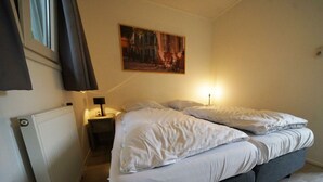 A bedroom with a bed, a nightstand, a lamp, a radiator, and a painting on the wall. - Holiday Home in Velsen-zuid With Terrace (Velsen-Zuid)