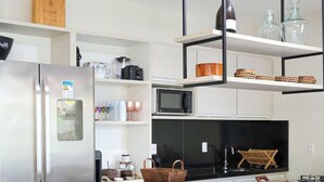 A modern kitchen with a stainless steel refrigerator, microwave, and a wooden dining table with chairs. - Condominio Fontes da Pipa (Tibau do Sul)
