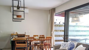 A dining area with a table and chairs, a hanging light fixture, and a view of a pool through a large window. - Condominio Fontes da Pipa (Tibau do Sul)