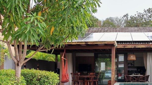 A covered outdoor dining area with a table and chairs, a hanging chair, and a view of the interior. - Condominio Fontes da Pipa (Tibau do Sul)