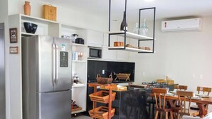 A modern kitchen with a refrigerator, microwave, and dining area with wooden chairs and a table. - Condominio Fontes da Pipa (Tibau do Sul)