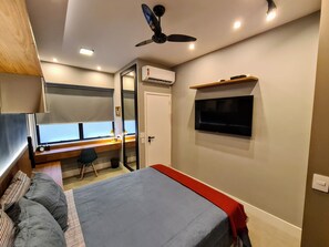 A bedroom with a bed, a desk with a computer, a TV, and a ceiling fan. - Studio do Arquiteto 1 (Rio de Janeiro)