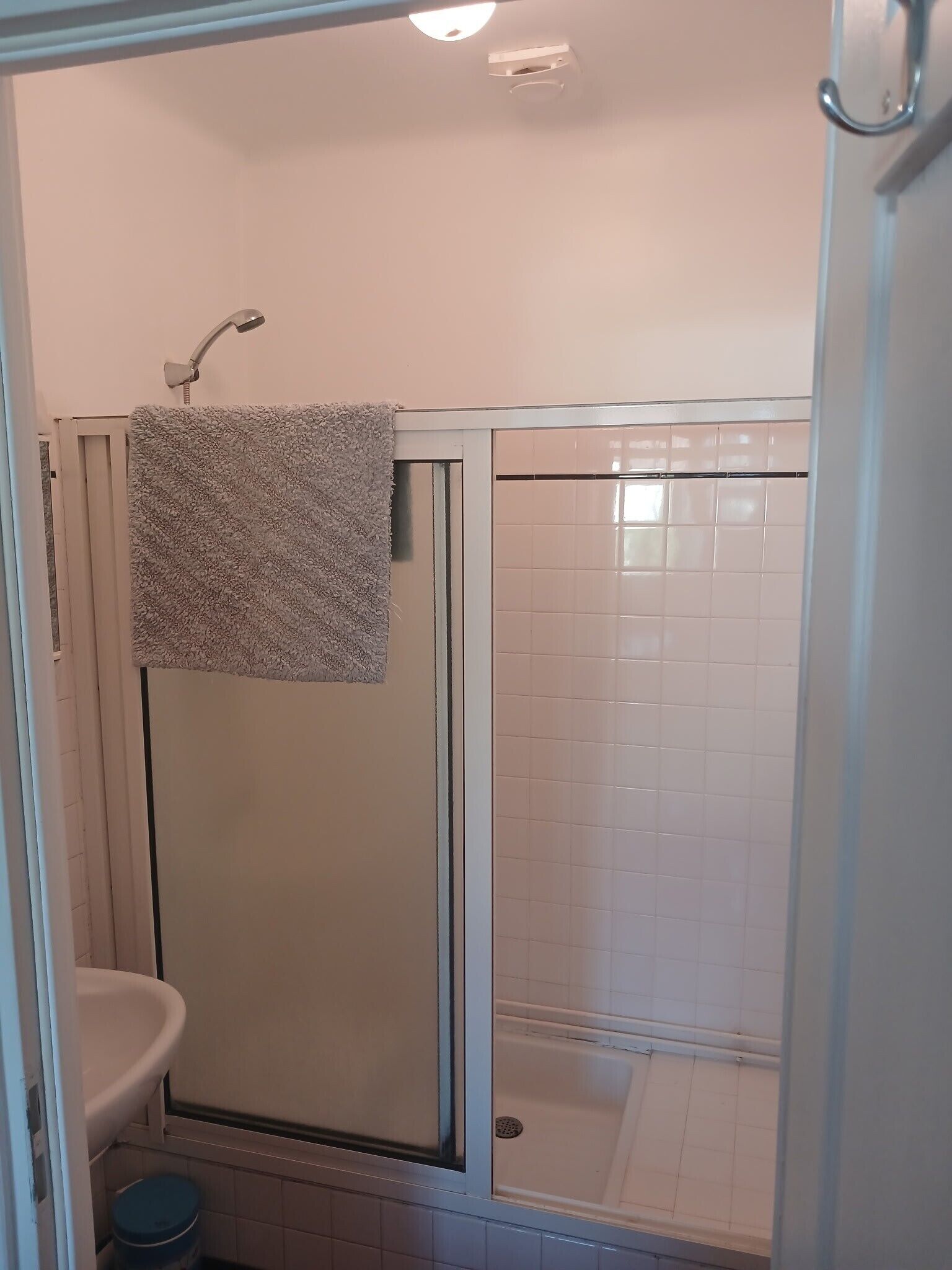A bathroom with a glass-enclosed shower, a white sink, and a towel hanging on the shower door.