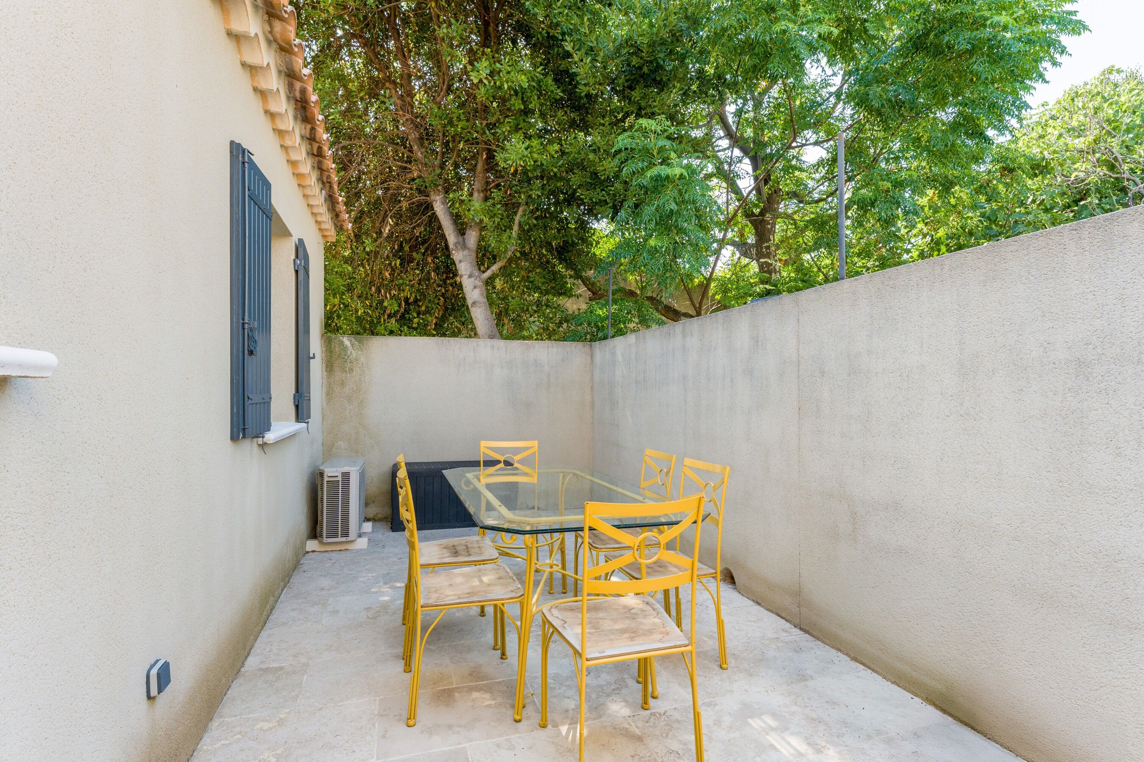 A small outdoor patio with a table and chairs, a window with shutters, and a wall with a textured surface.