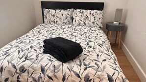 A bed with a floral bedspread, a black throw pillow, and a bedside table with a lamp.