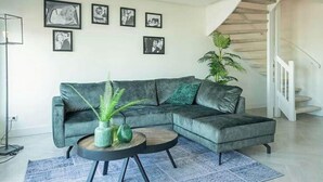 A modern living room with a sectional sofa, a round coffee table, and a staircase. - Zuiderzee Sauna 4 (Uitdam)