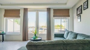 A modern living room with a sofa, a small table with a plant, and large windows with curtains. - Zuiderzee Sauna 4 (Uitdam)