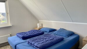 Un dormitorio con techo inclinado, una ventana, una mesita de noche con lámpara y una cama con ropa de cama azul.