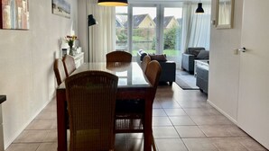 Un área de comedor con una mesa, sillas, un sofá y una ventana que ofrece vistas a casas.