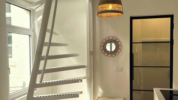 En modern inredning med en trappa, en hängande lampa, en spegel och ett köksområde.