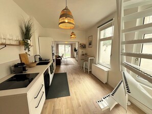Eine moderne Küche mit einer zentralen Kochinsel, einem Essbereich mit Hockern und einem großen Fenster für natürliches Licht.