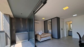 A modern hotel room with a large bed, a sliding door closet, and a bathroom visible through an open door. - Estúdio com piscina e academia no rooftop (São Paulo)