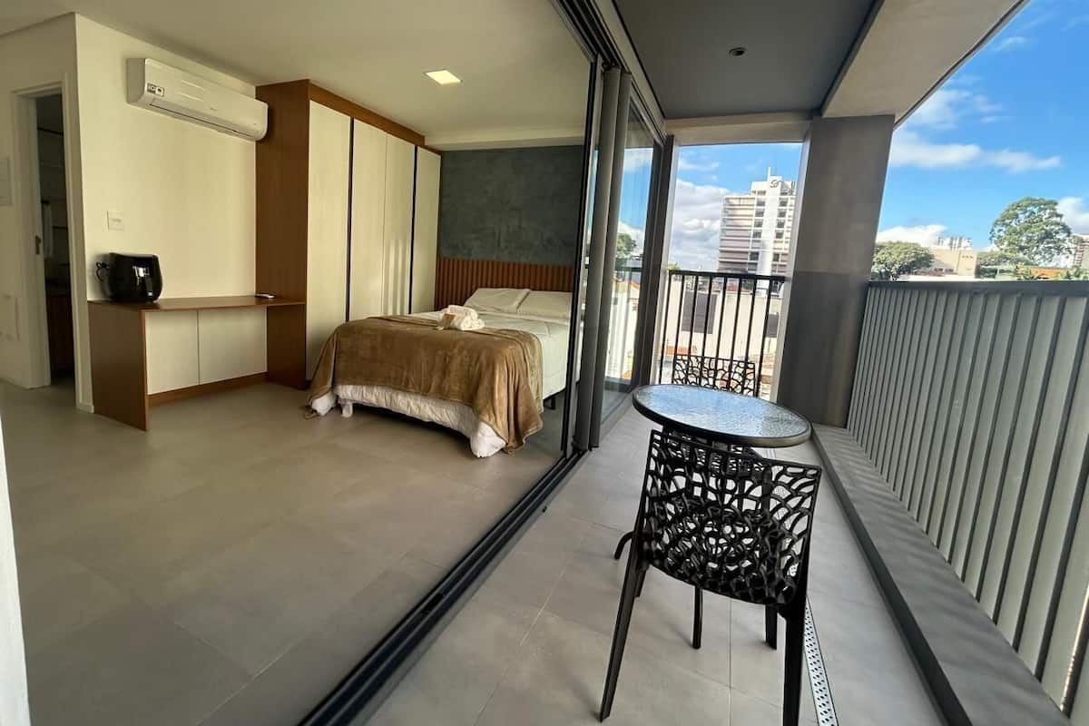 A balcony with a bed, a small table, and an air conditioning unit.