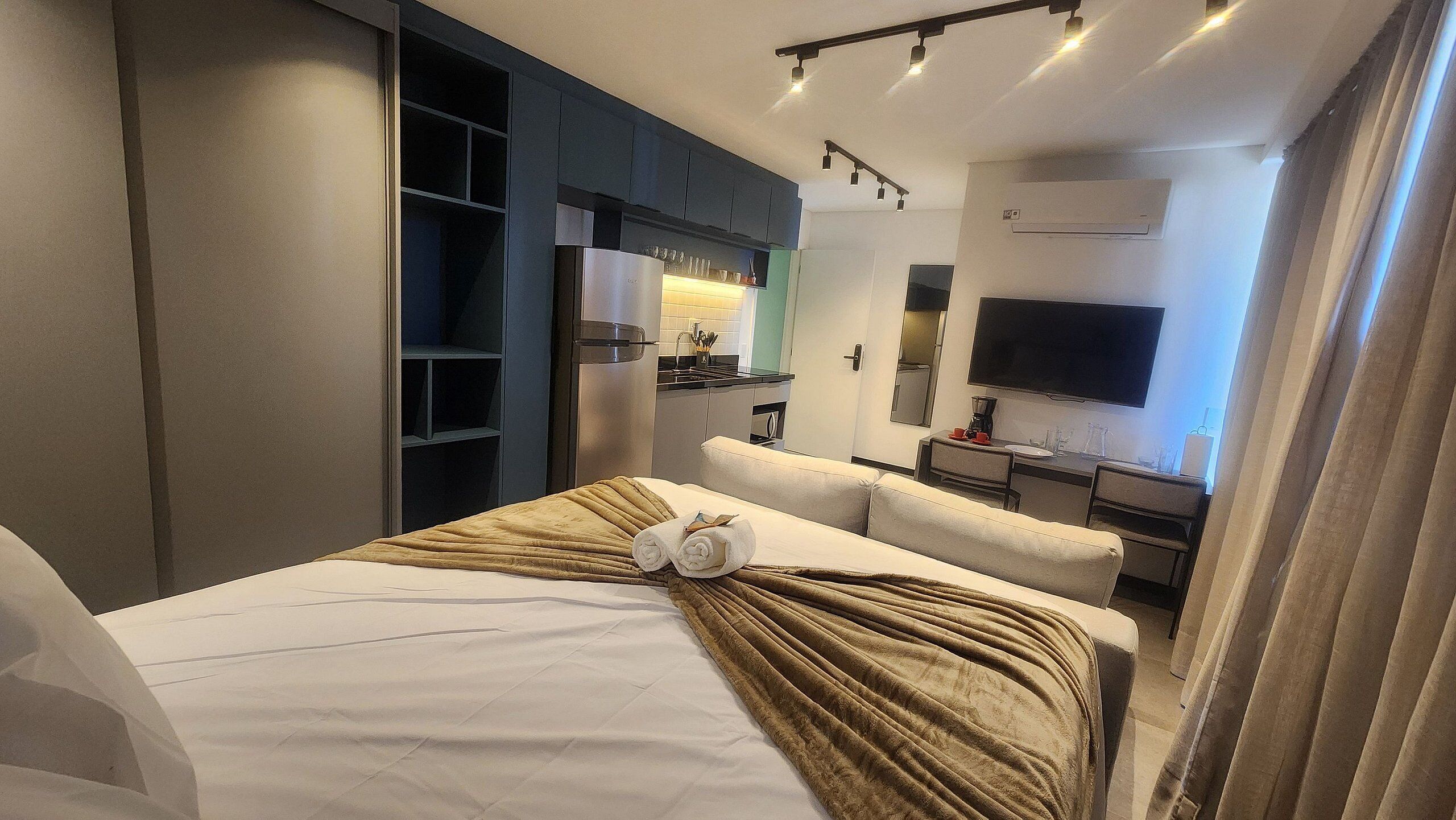 A hotel room with a bed, a sofa, a kitchenette, and a TV.