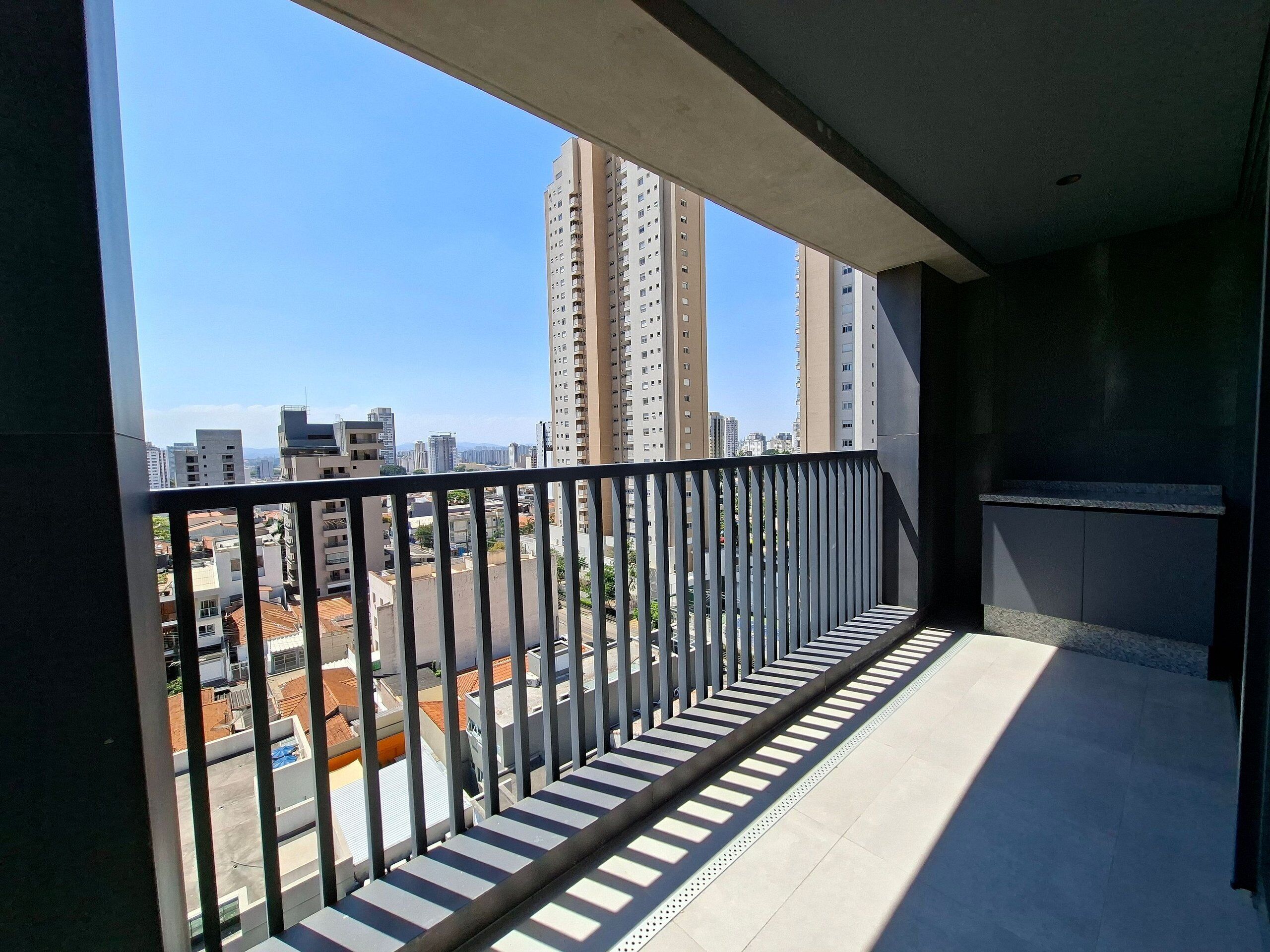 A balcony with a metal railing, a tiled floor, and a view of high-rise buildings in the distance.
