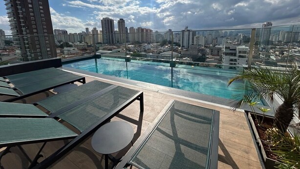 A rooftop pool with lounge chairs and a city view. - Estúdio com piscina e academia no rooftop (São Paulo)