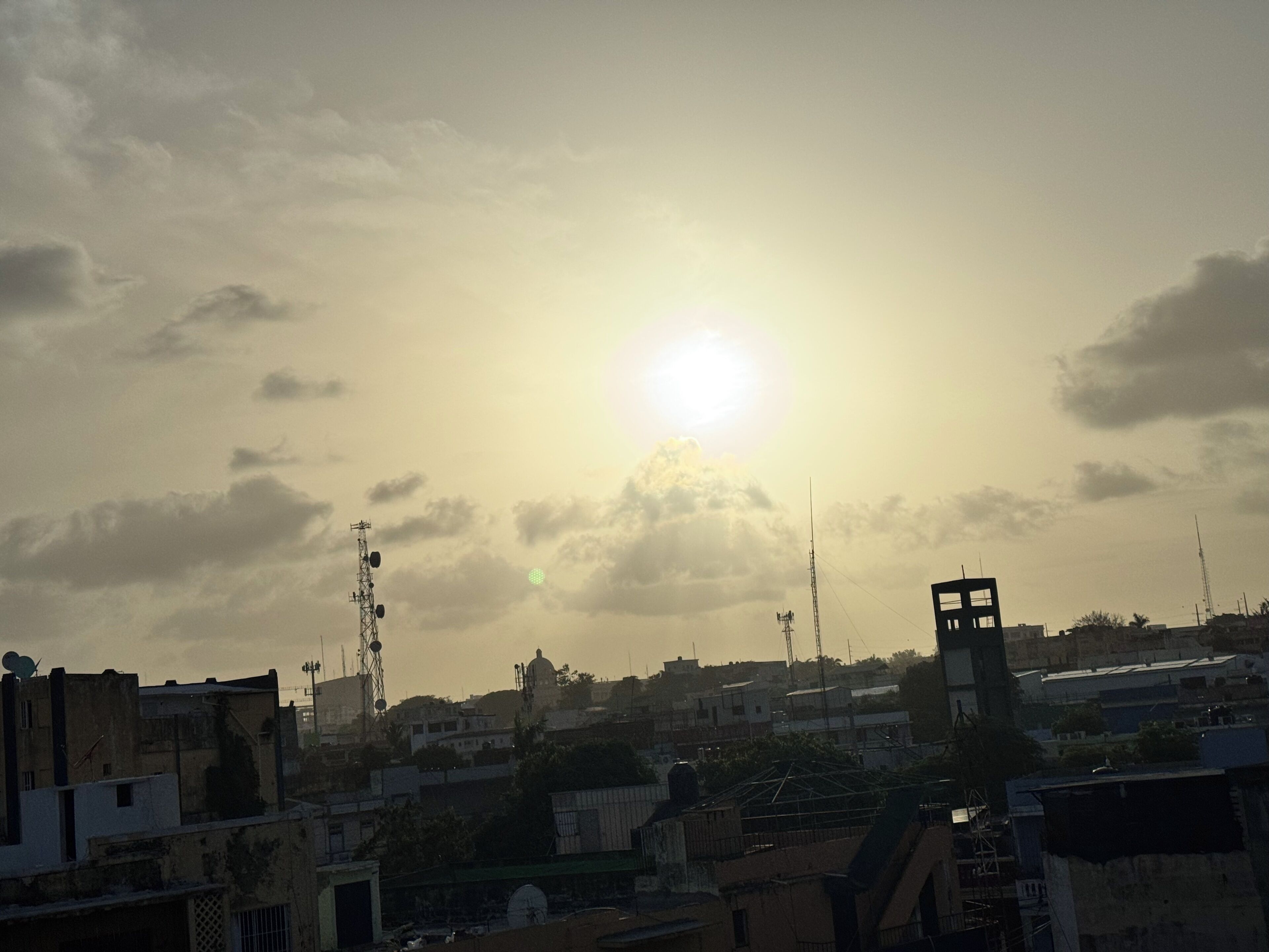 Une vue urbaine avec des bâtiments, une tour imposante, et le soleil se couchant ou se levant dans le ciel.